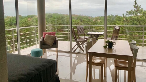 Un balcón con mesa y sillas, un sofá y vistas a un paisaje boscoso.