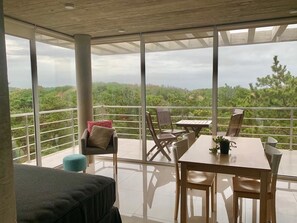 A balcony with a table and chairs, a sofa, and a view of a forested landscape. - Casiopea (Mar de Las Pampas)