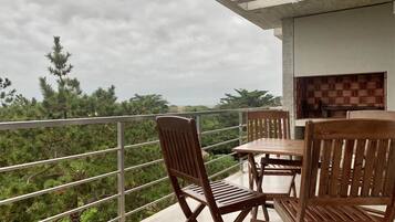A balcony with a table and chairs, overlooking a forested area.