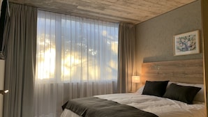 Habitación de hotel con una cama grande, un cabecero de madera, un cuadro en la pared y cortinas de encaje en la ventana.