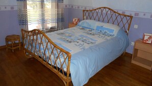 Un dormitorio con estructura de cama de madera, colcha azul y ventana con cortinas a rayas.