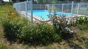 Una piscina rodeada por una cerca blanca, con flores y césped en primer plano.