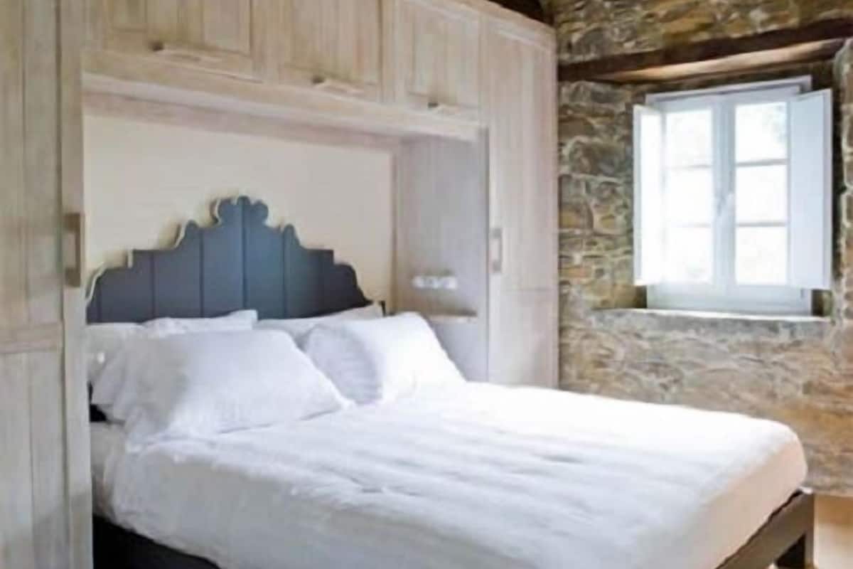 Makuuhuone, jossa on sänky, puupalkit, kiviseinä ja ikkuna.