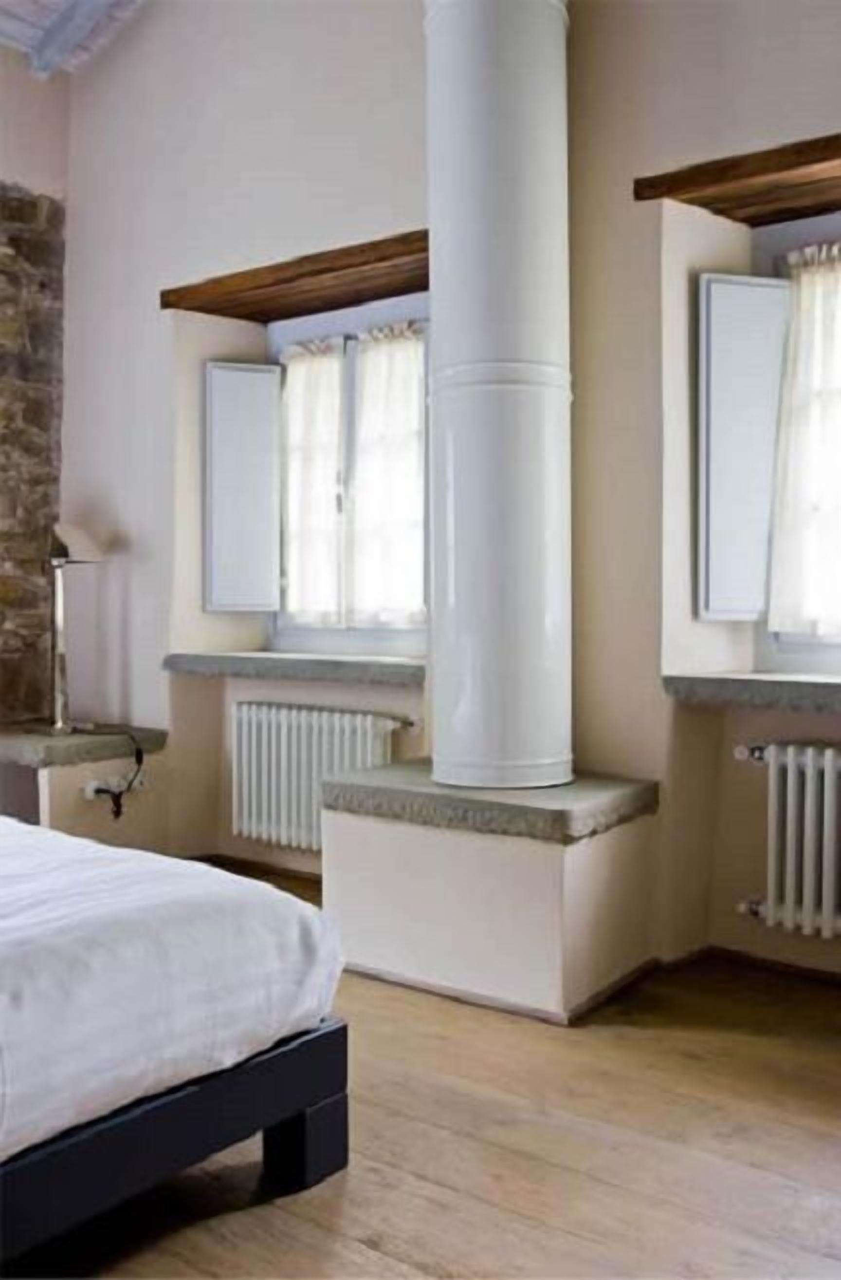 A bedroom with a bed, a stone wall, a white radiator, and a window with curtains.