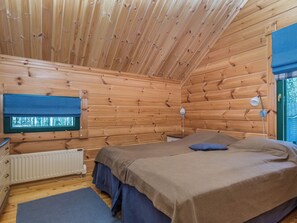 A wooden cabin bedroom with a bed, bedside lamps, a window, and a radiator. - Villa populus by Interhome (Pertunmaa)