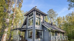 A two-story wooden house with a balcony, surrounded by trees.