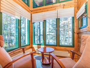 L’intérieur d’une cabane, avec de grandes fenêtres, des meubles en bois et une vue sur une forêt.