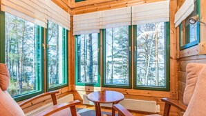 A cozy cabin interior with large windows, wooden walls, and a round table.
