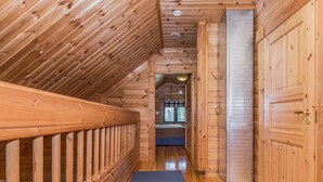 A wooden interior with a sloped ceiling, a blue mat leading to a bed, and wooden doors.