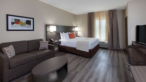 A hotel room with a bed, a sofa, a desk, a chair, a TV, and a framed picture on the wall. - Hawthorn Extended Stay by Wyndham Odessa (Odessa)