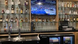 A bar area with shelves of liquor bottles, a television displaying a sports event, a cash register, and a refrigerator stocked with beverages. - Hawthorn Extended Stay by Wyndham Odessa (Odessa)