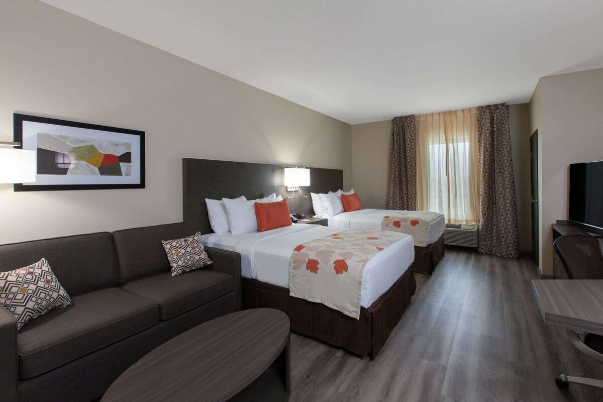 A hotel room with a sofa, two beds, a desk, and a TV.