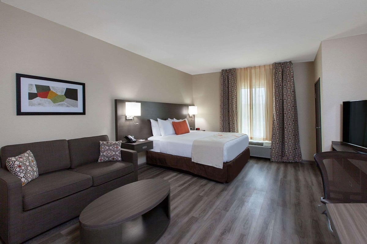 A hotel room with a bed, a sofa, a coffee table, a TV, and a framed picture on the wall.