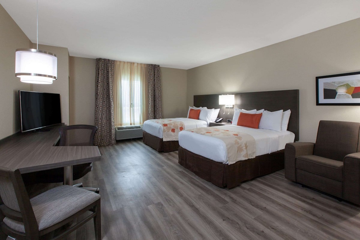 A hotel room with two beds, a desk, a chair, a TV, and a large window with curtains.