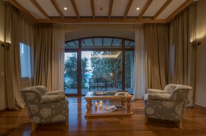 Una habitación con dos sillones, una mesa de centro de madera y un amplio ventanal con cortinas.