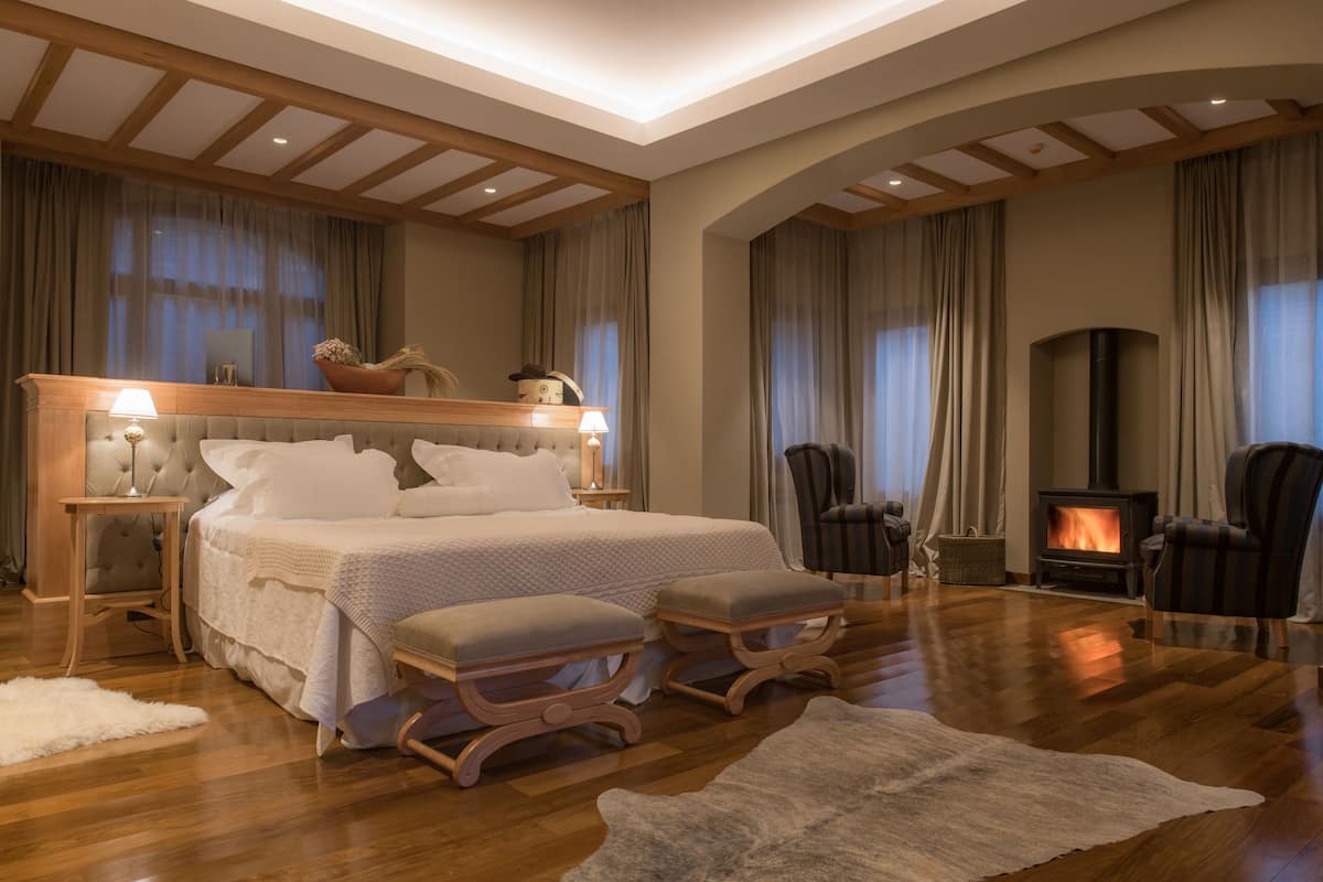 A spacious bedroom with a large bed, wooden beams, a fireplace, and a cozy seating area.