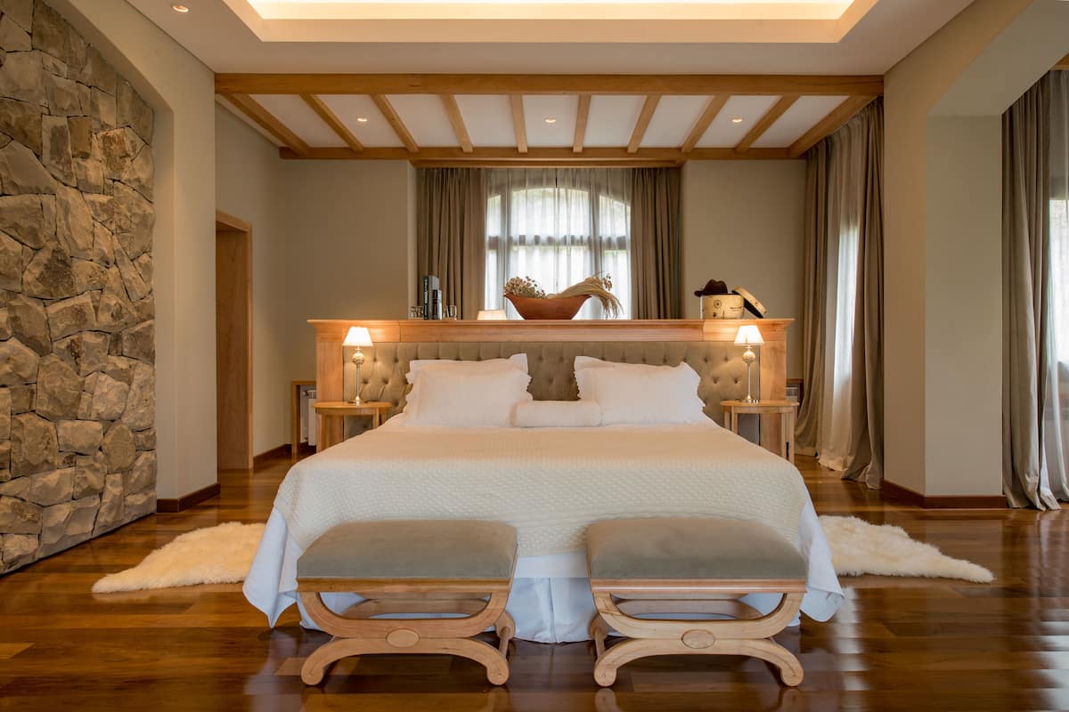 A large bed with a headboard, two bedside tables, and a stone wall.