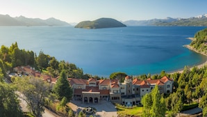 A large, multi-story building with a courtyard, surrounded by lush greenery and overlooking a large body of water with mountains in the background. - Villa Beluno Hotel & Spa, small luxury hotels of the world (San Carlos de Bariloche)