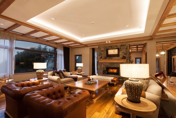 A spacious living room with a fireplace, leather sofas, and a large window offering a view of the outdoors. - Villa Beluno Hotel & Spa, small luxury hotels of the world (San Carlos de Bariloche)