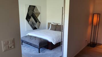 A bedroom with a bed, a bench, a wall-mounted artwork, and a floor lamp.