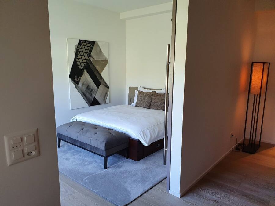 A bedroom with a bed, a bench, a wall-mounted artwork, and a floor lamp.