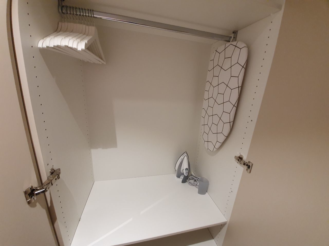 A small, white bathroom with a single shower, a white towel rack, and a white shower curtain with a geometric pattern.