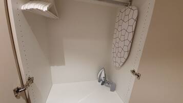A small, white bathroom with a single shower, a white towel rack, and a white shower curtain with a geometric pattern.