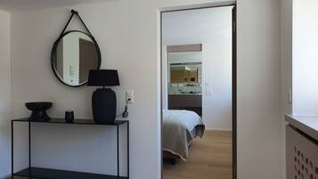 Un dormitorio moderno con cama, mesita de noche, espejo y consola con lámpara.