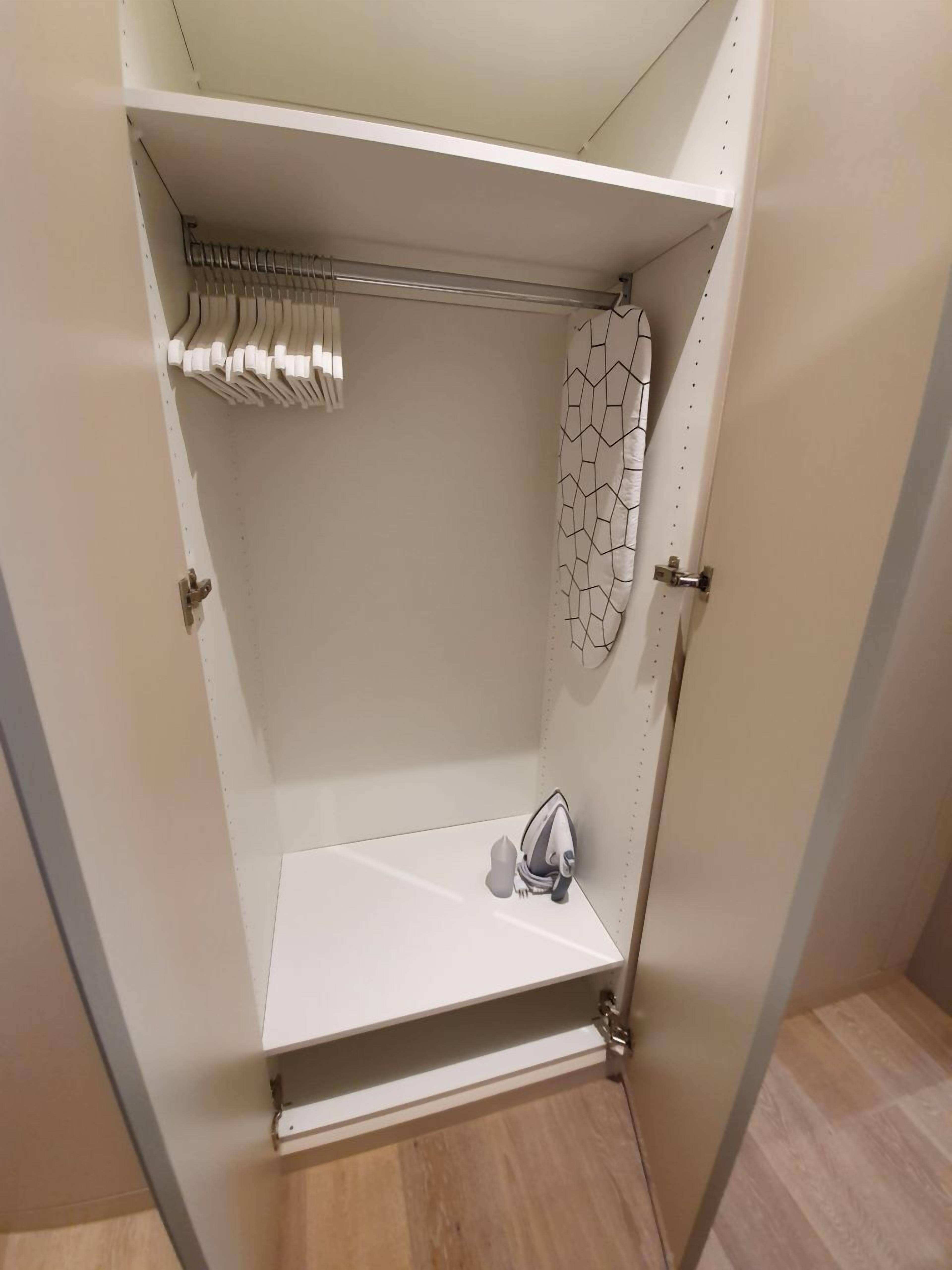 Un petit placard blanc, ouvert, muni d’une tringle et d’une étagère.