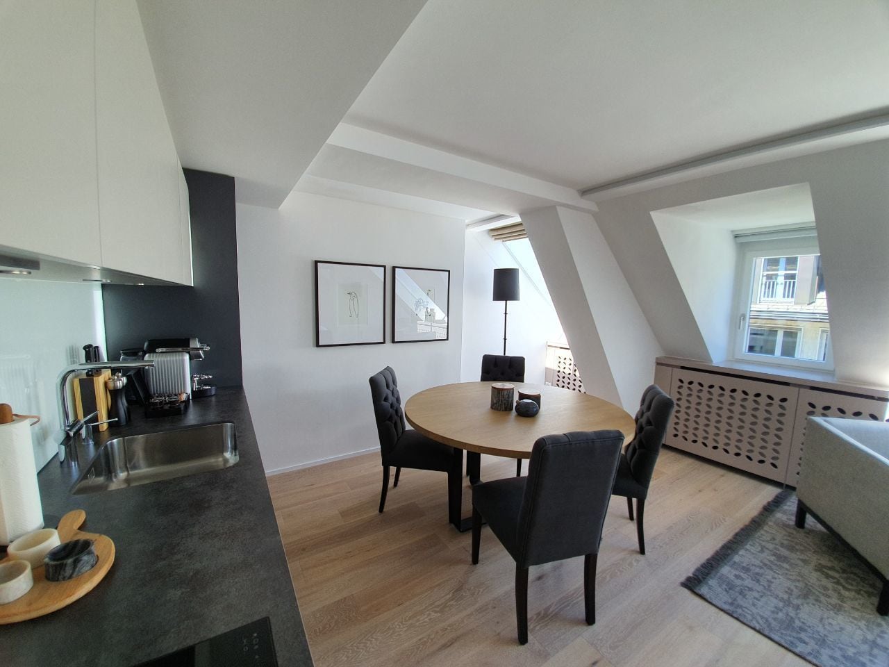 Eine moderne Küche mit Essbereich, ausgestattet mit einem runden Tisch und Stühlen, einer schwarzen Arbeitsplatte und einem Fenster für natürliches Licht.