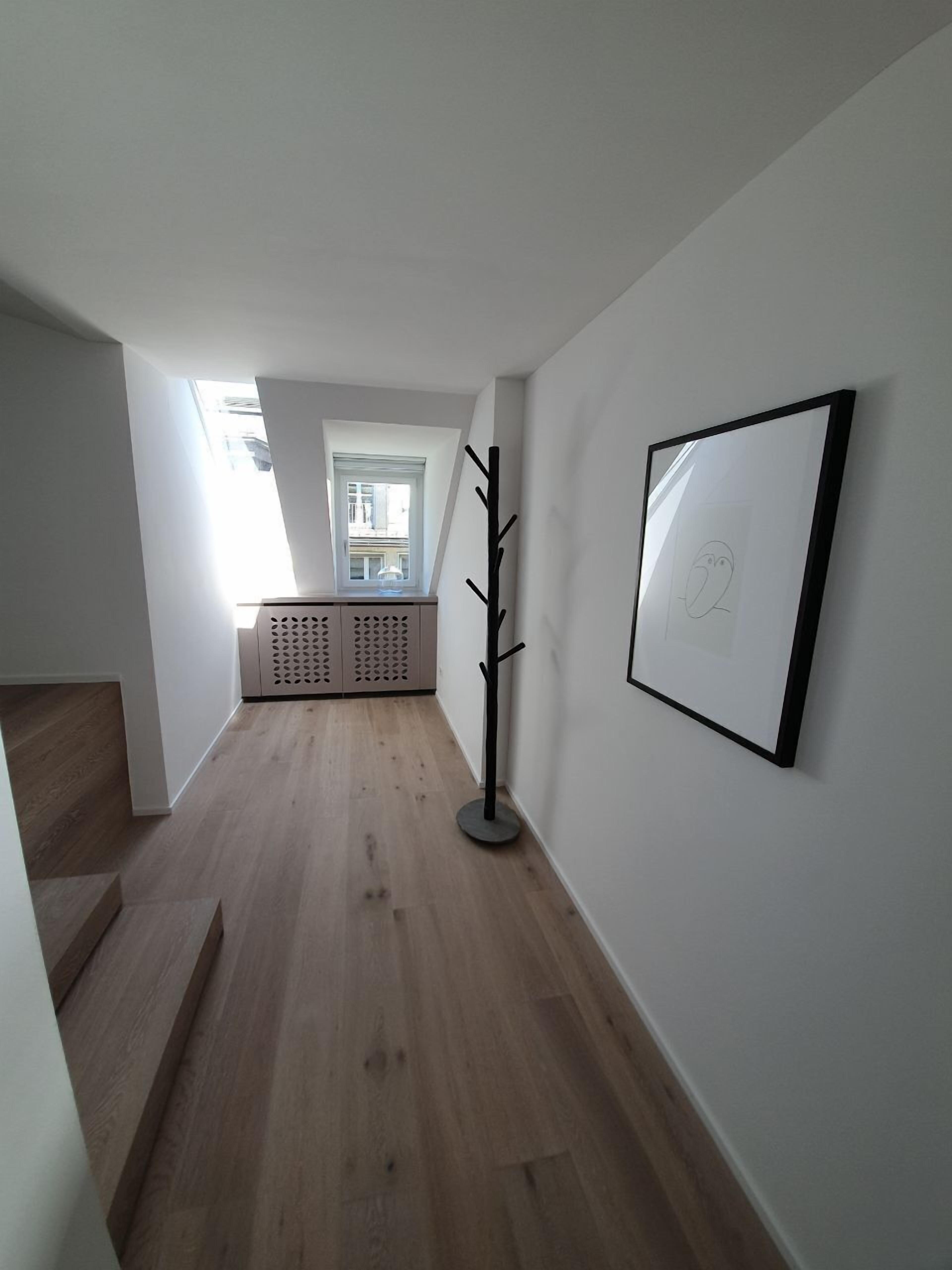 A hallway with wooden flooring, a coat rack, a framed picture, and a window with a view of the outside.