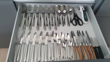 Eine Schublade mit verschiedenen Besteckstücken, darunter Gabeln, Messer und Löffel, sowie eine Schere.
