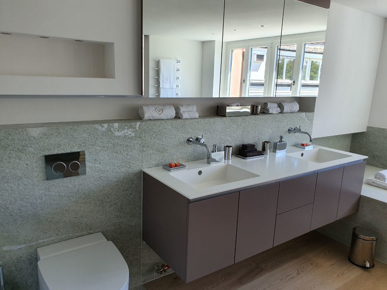 A modern bathroom with a double sink, a toilet, and a large mirror.
