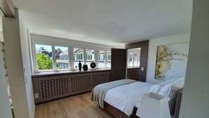 Een slaapkamer met een bed, een raam met uitzicht op gebouwen, een radiator en een schilderij aan de muur.
