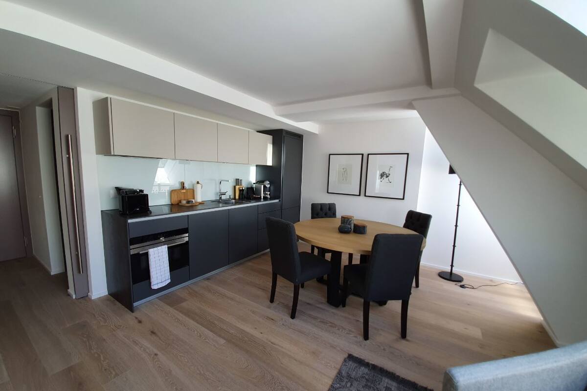 Een moderne keuken met donkere kastjes, een eettafel met stoelen en een lichte houten vloer.