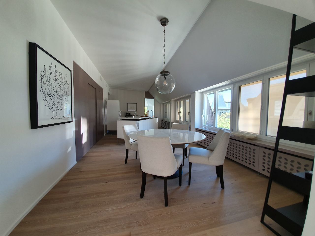A spacious dining area with a round table and chairs, a pendant light, and large windows providing natural light.