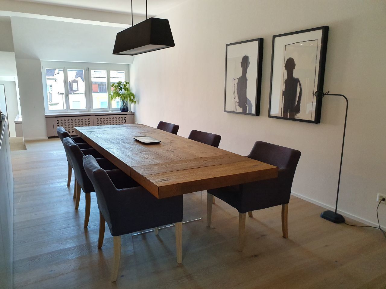 A dining area with a wooden table, six chairs, and two framed artworks on the wall.