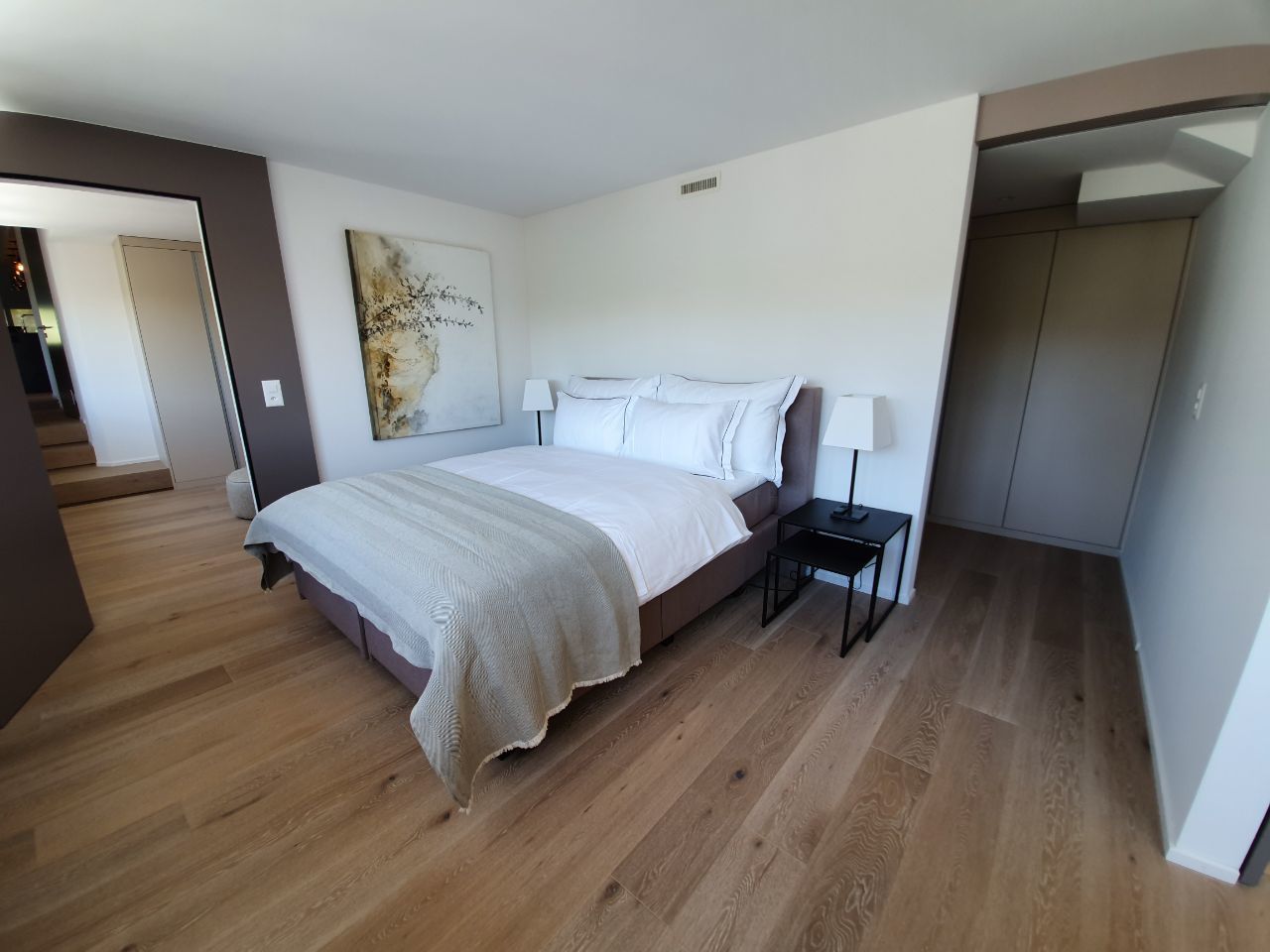 A modern bedroom with a bed, bedside table, and a painting on the wall.