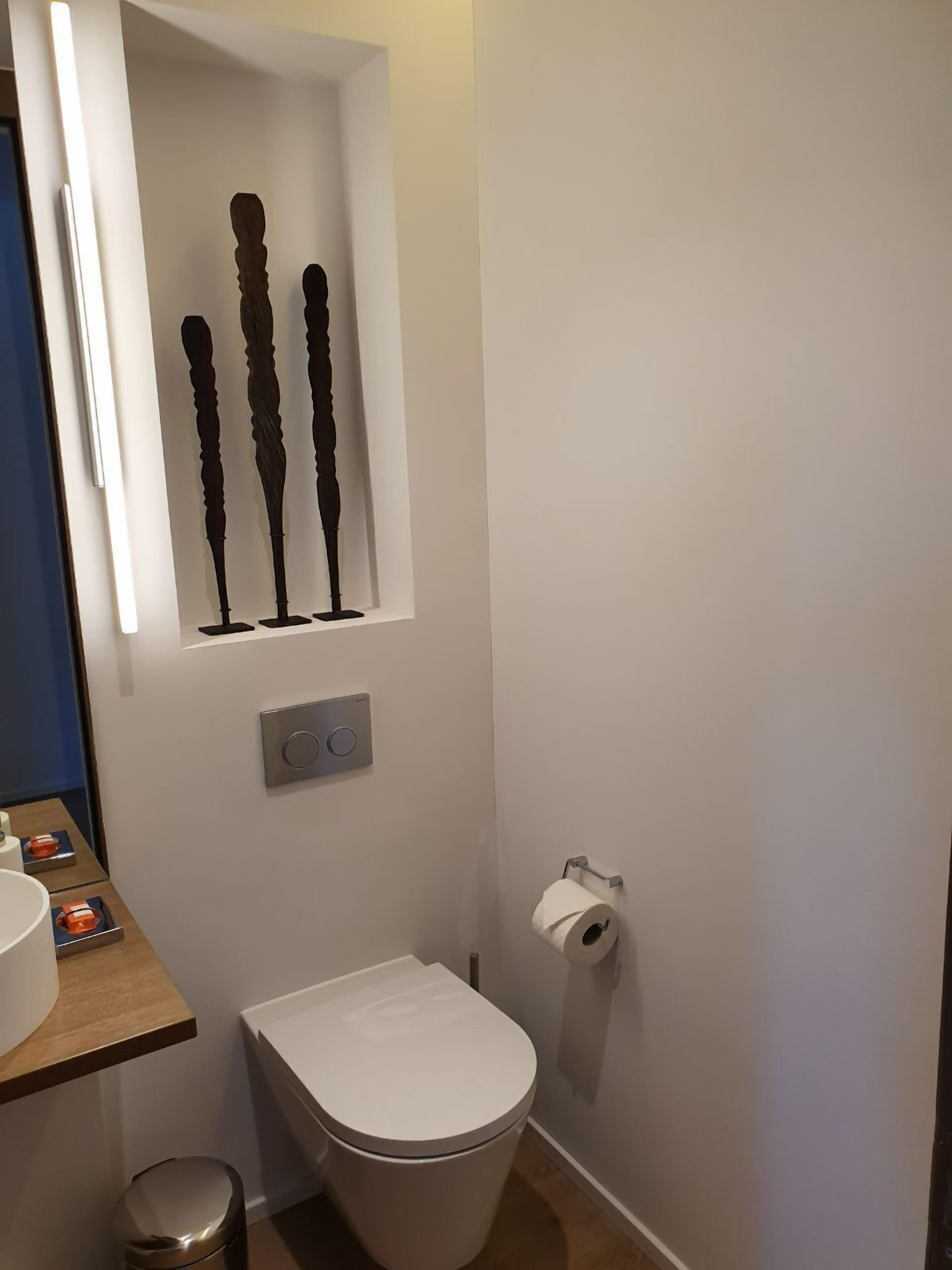 Uma casa de banho pequena com sanita, lavatório e uma estante com objetos decorativos.