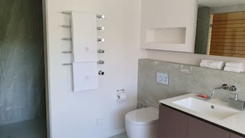 Ein modernes Badezimmer mit einer weißen Toilette, einem Waschbecken mit Spiegel und einem Handtuchhalter mit mehreren Handtüchern.