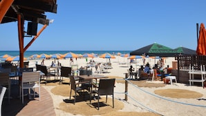 Een restaurant aan het strand met terras, parasols en uitzicht op het strand.