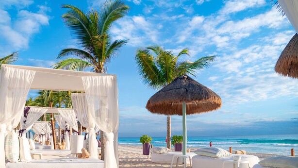 A beachside resort with a canopy bed, lounge chairs, and a thatched umbrella.