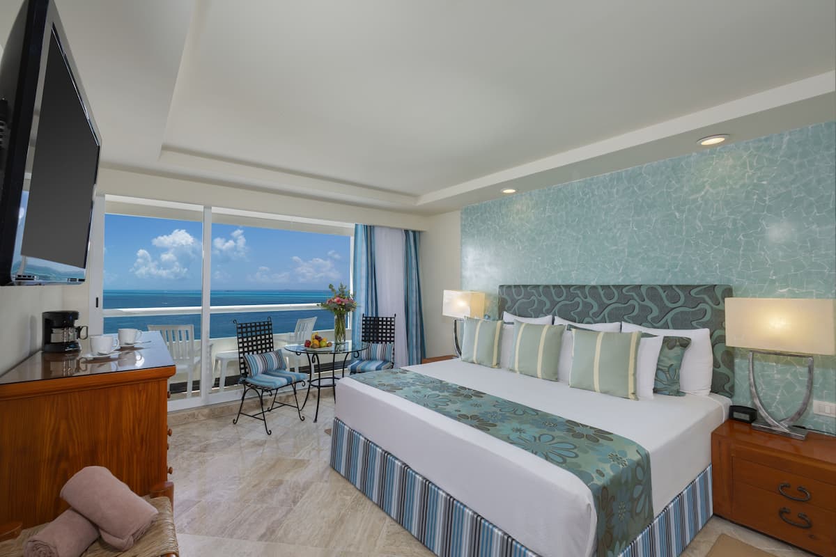 Ein Hotelzimmer mit einem großen Bett, einem Schreibtisch mit Kaffeemaschine, einem Sessel und Blick aufs Meer.