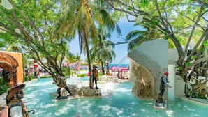 A tropical resort pool area with statues, palm trees, and a clear blue sky.
