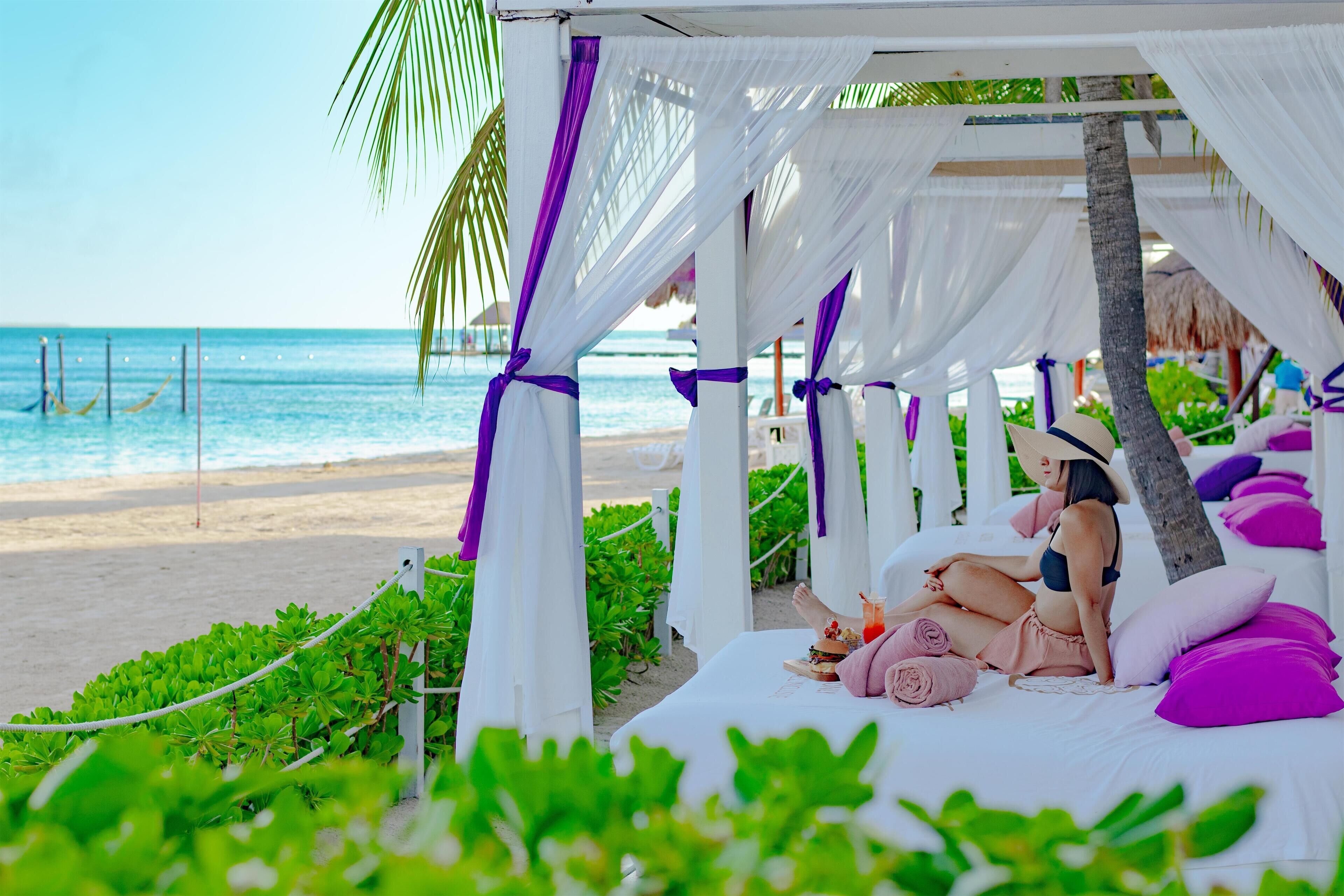 Una cabaña frente al mar con cama, almohadas y una bebida.