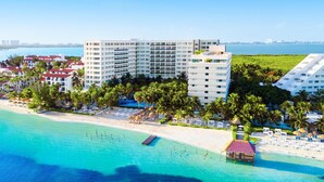 A beachfront hotel with multiple floors, a beach, and palm trees.