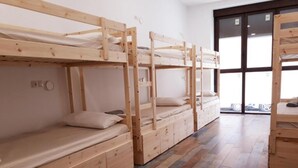 A row of bunk beds with storage drawers, a wooden floor, and a large window with a view of parked cars. - Hub Hostel Seville (Seville)