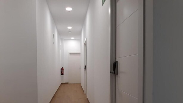 A long, narrow hallway with white walls and wooden flooring, leading to a door at the end. - Hub Hostel Seville (Seville)