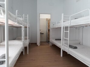 A dormitory room with bunk beds, a wooden floor, and a door leading to a bathroom. - Hub Hostel Seville (Seville)