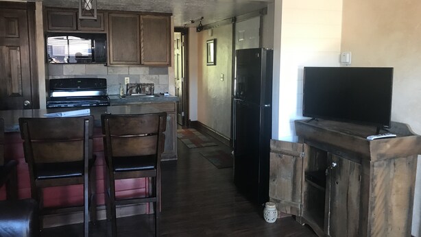 A kitchen with wooden cabinets, a refrigerator, a dining area with chairs, and a television on a wooden stand. - North Wind Condo (Angel Fire)